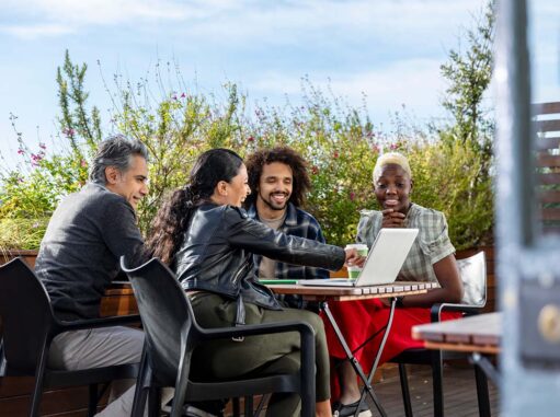 Group of people sitting outside talking and pointing at a computer