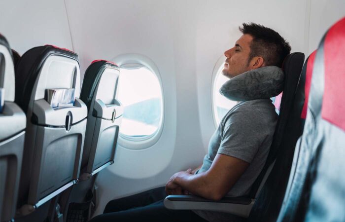 Man on airplane with neck pillow.