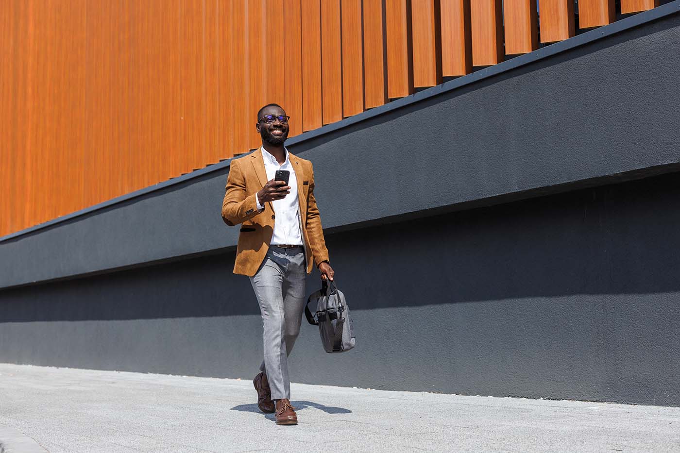 Business professional walking with a laptop bag while using a mobile phone.